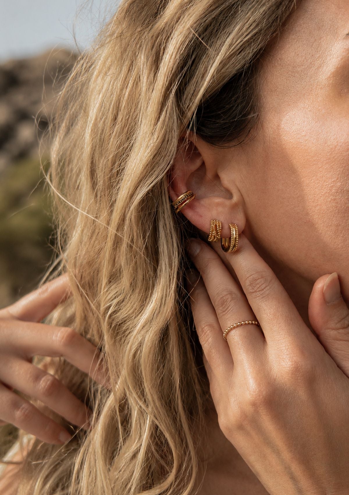 Mini créoles Étreinte Organique portées à l'oreille en accumulation avec un ear cuff doré, bagues spirale et texturée perlée Namaka portées à la main
