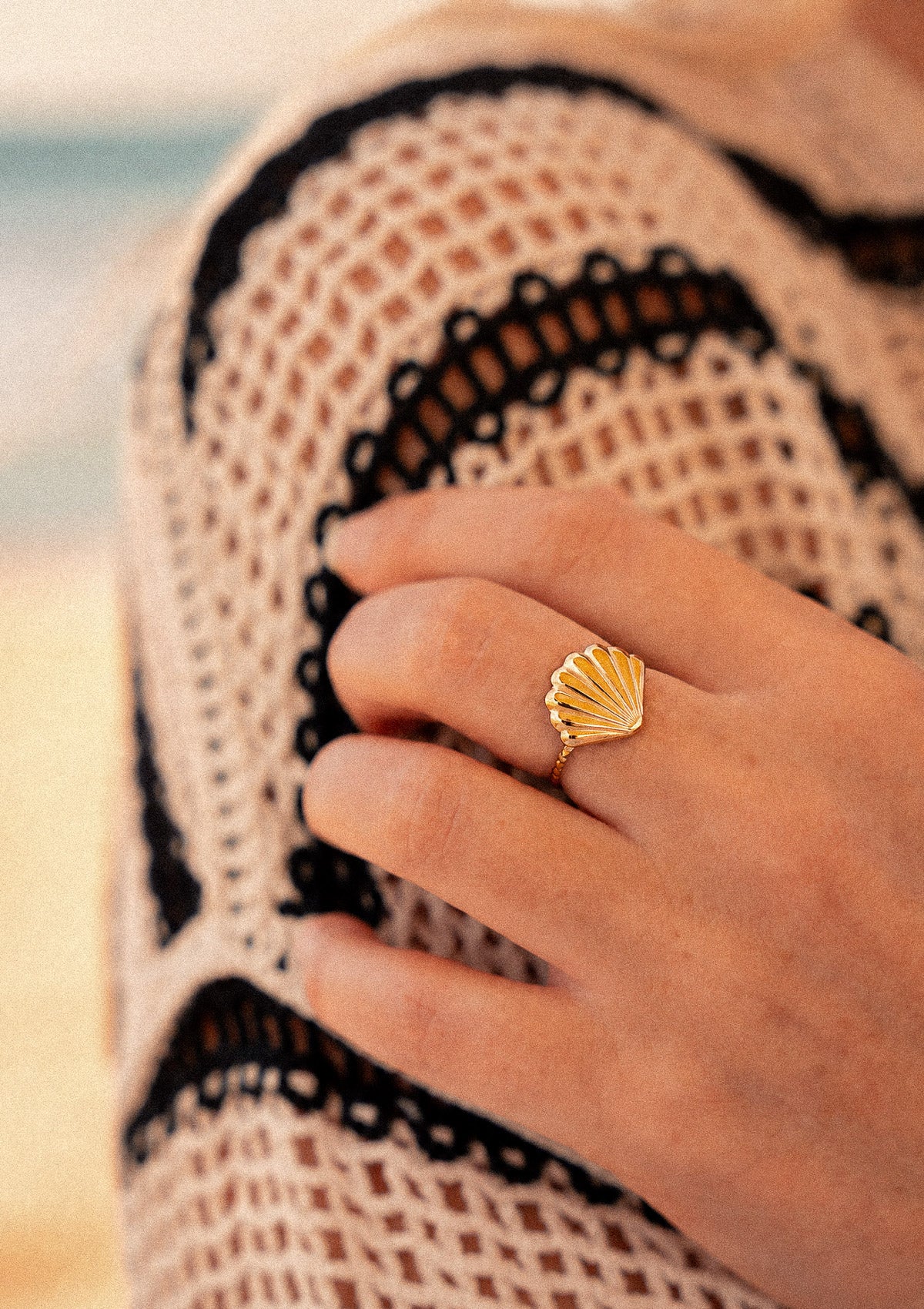 Bague Coquillage Les Jours Salés portée avec robe crochet en filet en bord de plage, coquille dorée à cannelures rayonnantes signature Namaka collection Solaire