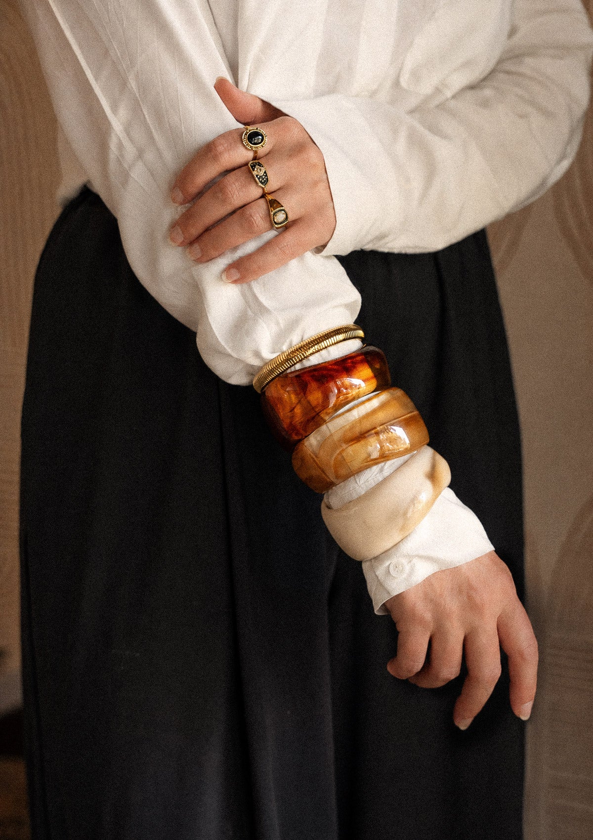 Trois bracelets jonc résine acrylique caramel miel ivoire portés en accumulation avec jonc acier doré strié, chemise blanche