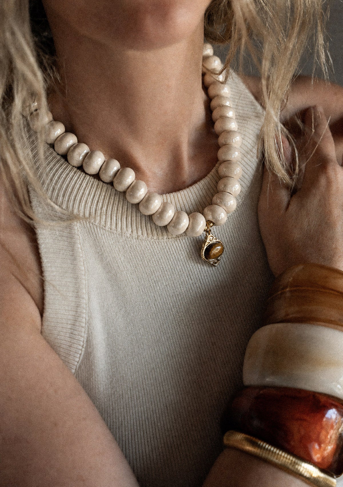 Collier ras-de-cou céramique crème et Œil de Tigre porté sur débardeur crème avec accumulation joncs résine caramel ivoire et jonc doré