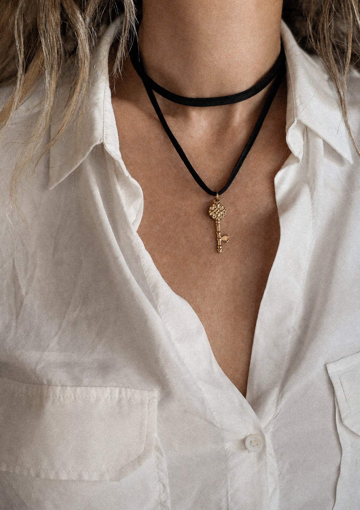 Collier ruban satin noir avec pendentif clé dorée porté en choker au cou sur chemise blanche