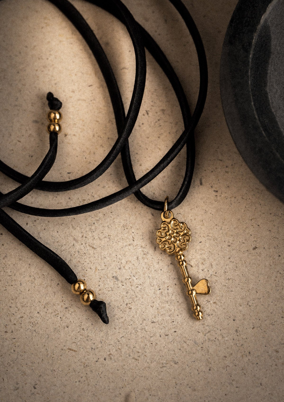 Packshot pendentif clé dorée style ancien à anse ouvragée cœur sur ruban satin noir extrémités perles dorées, assemblé en France