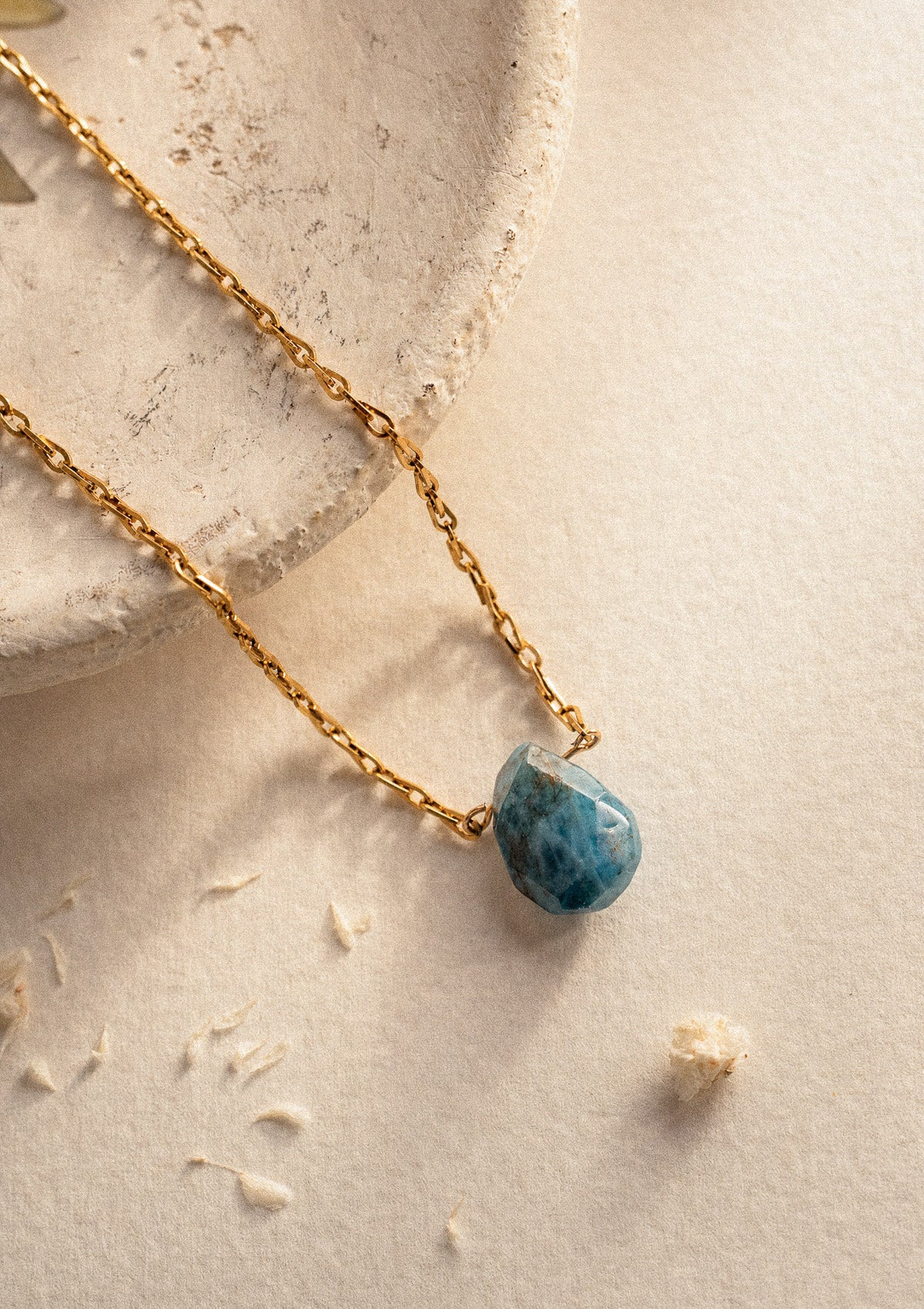Gros plan pierre d'Apatite néon brute facettée sur chaîne fine dorée, détail collier Éclat Brut sur plâtre naturel – Namaka collection Solaire, assemblé en France