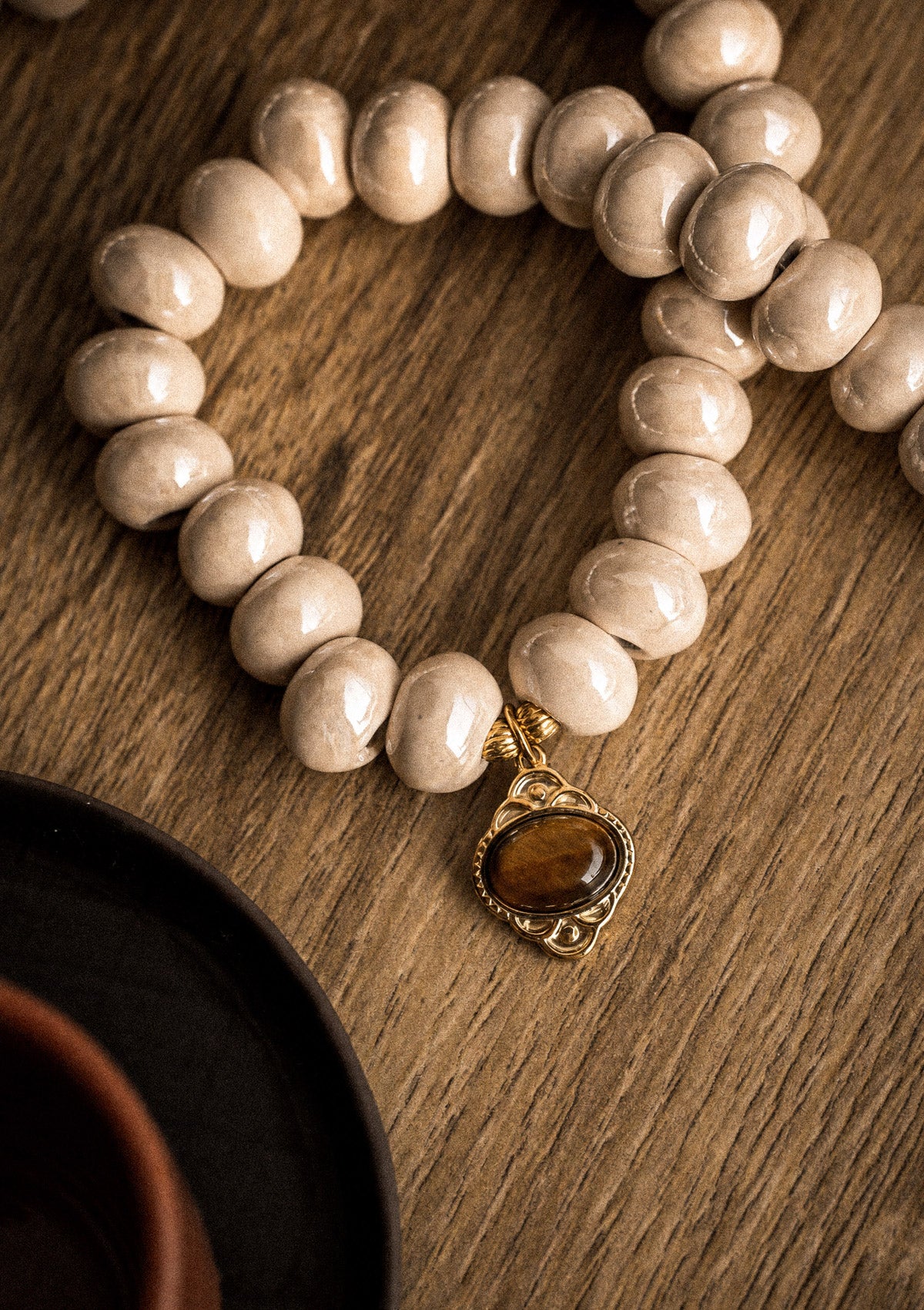Packshot collier ras-de-cou perles céramique émaillée crème et pendentif Œil de Tigre cabochon ovale monture dorée, assemblé en France