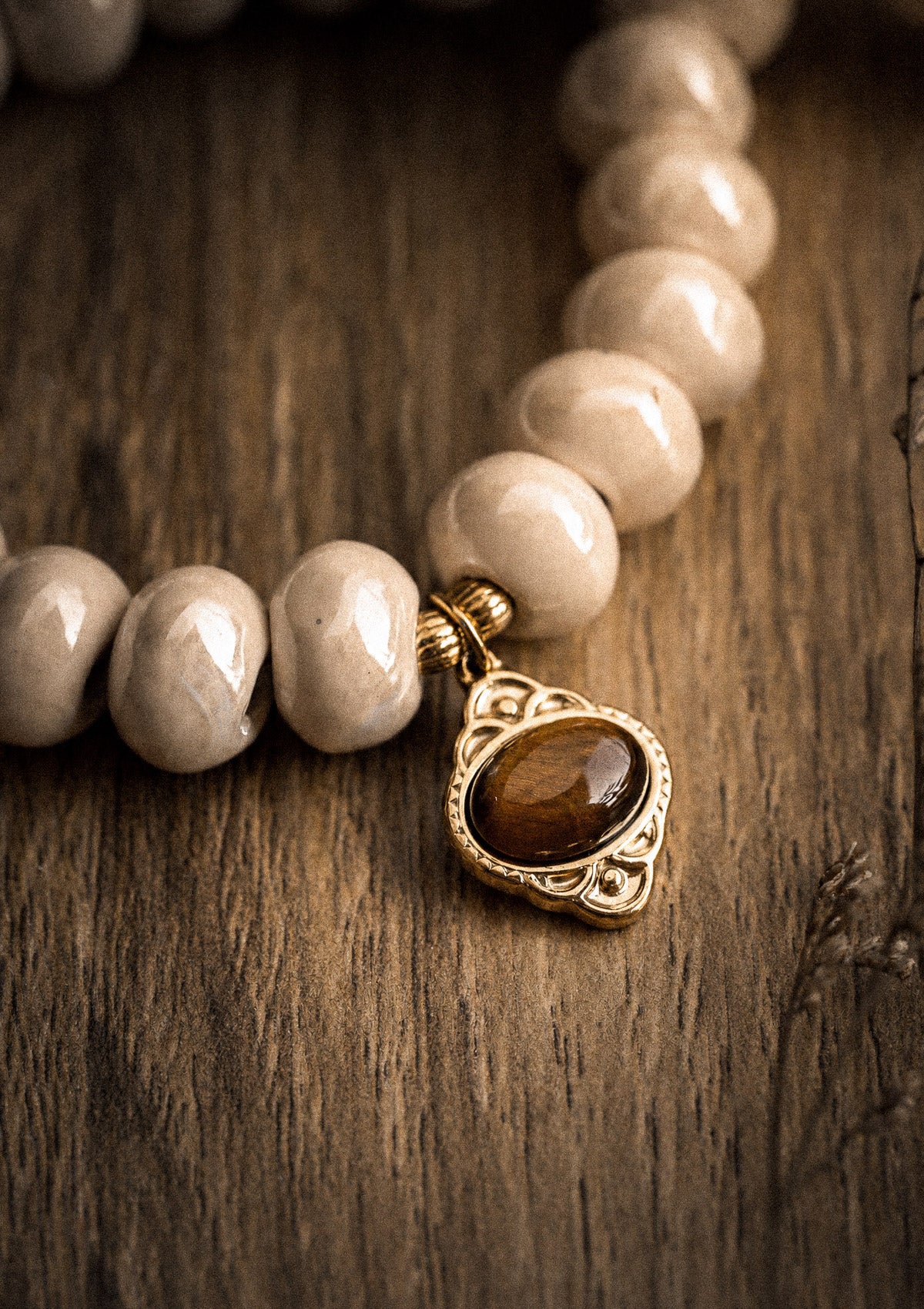 Gros plan pendentif Œil de Tigre cabochon ovale brun fauve serti monture dorée feuillagée, perles céramique émaillée crème