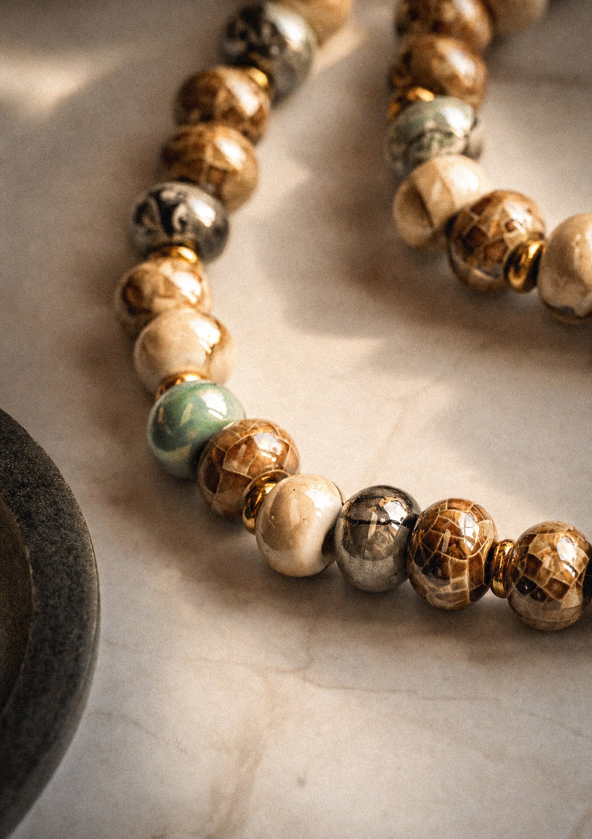 Détail perles céramique émaillée motif quadrillé brun doré ivoire gris marbré et vert amande, collier assemblé en France