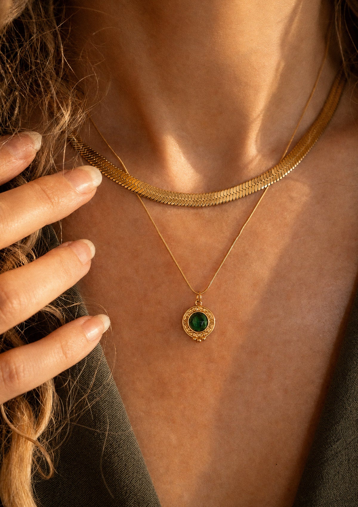 Détail du collier Malachite porté au cou, pendentif rond vert profond serti en or et chaîne serpent plate signé Namaka