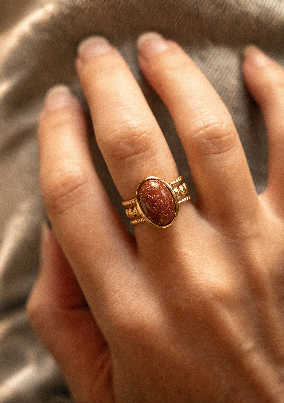 Bague Pierre de Sable Lumière Intérieure portée au doigt, cabochon ovale aux reflets cuivrés scintillants en or recyclé 18 carats Namaka