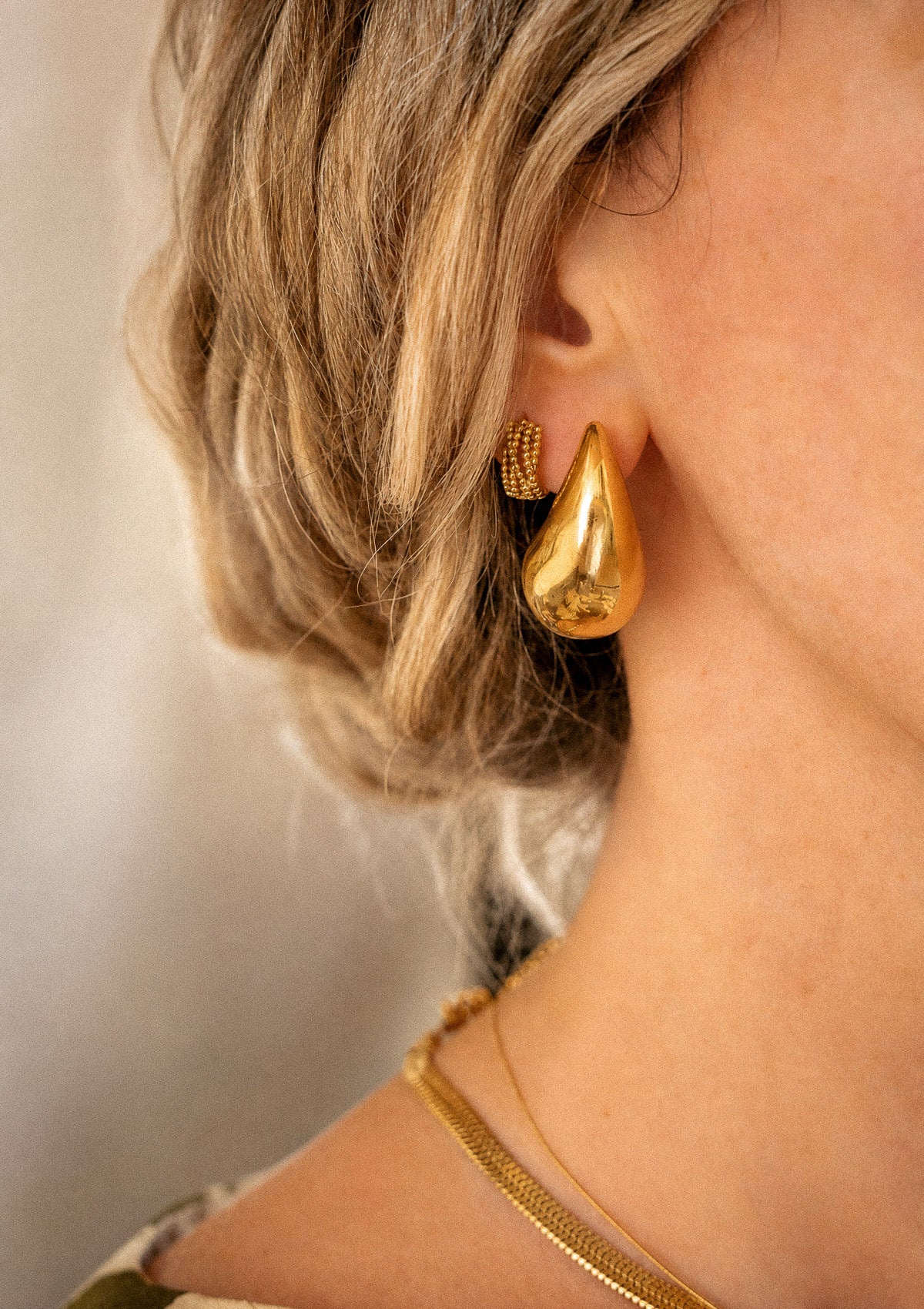 Boucles d'oreilles gouttes Vague Organique dorées portées à l'oreille en duo avec une mini créole perlée Étreinte Organique et un collier serpent plate Namaka