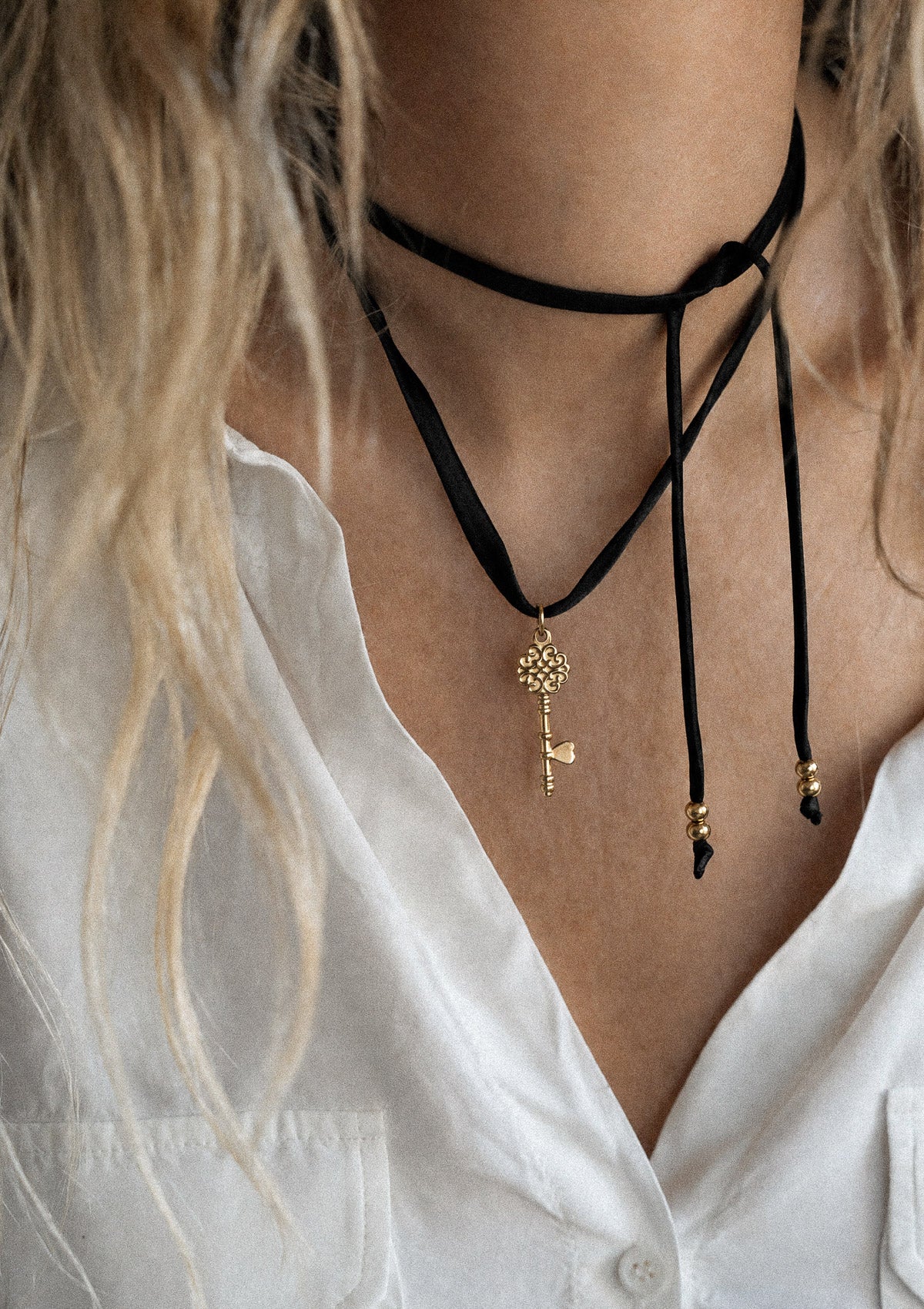 Collier ruban satin noir avec pendentif clé dorée porté en double au cou sur chemise blanche, longueur ajustable
