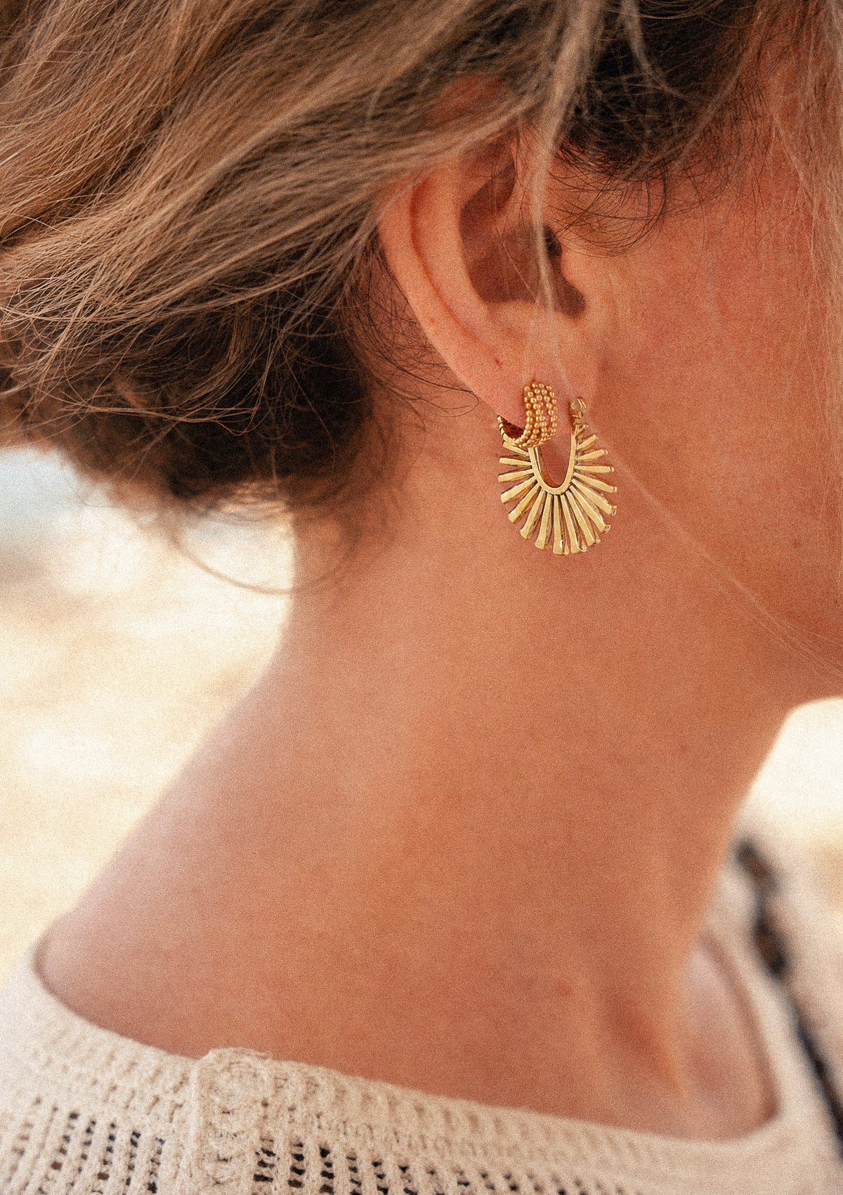 Boucles Soleil Rayonnant portées à l'oreille en bord de plage, éventail doré à rayons de soleil et créole perlée en accumulation lumière chaude – Namaka collection Solaire