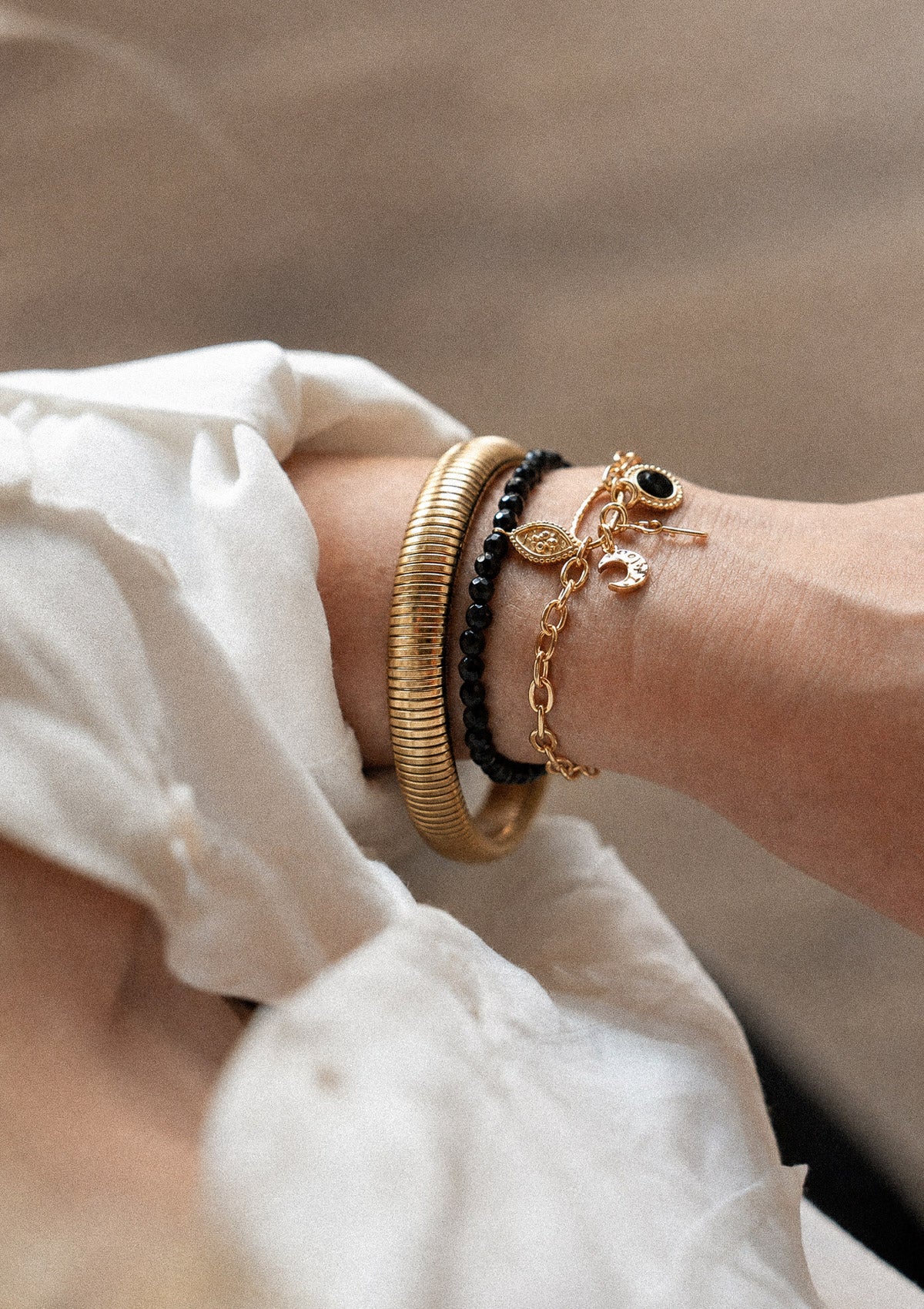 Bracelet jonc souple acier inoxydable doré strié Ligne Dorée porté au poignet en accumulation avec joncs résine et perles Onyx
