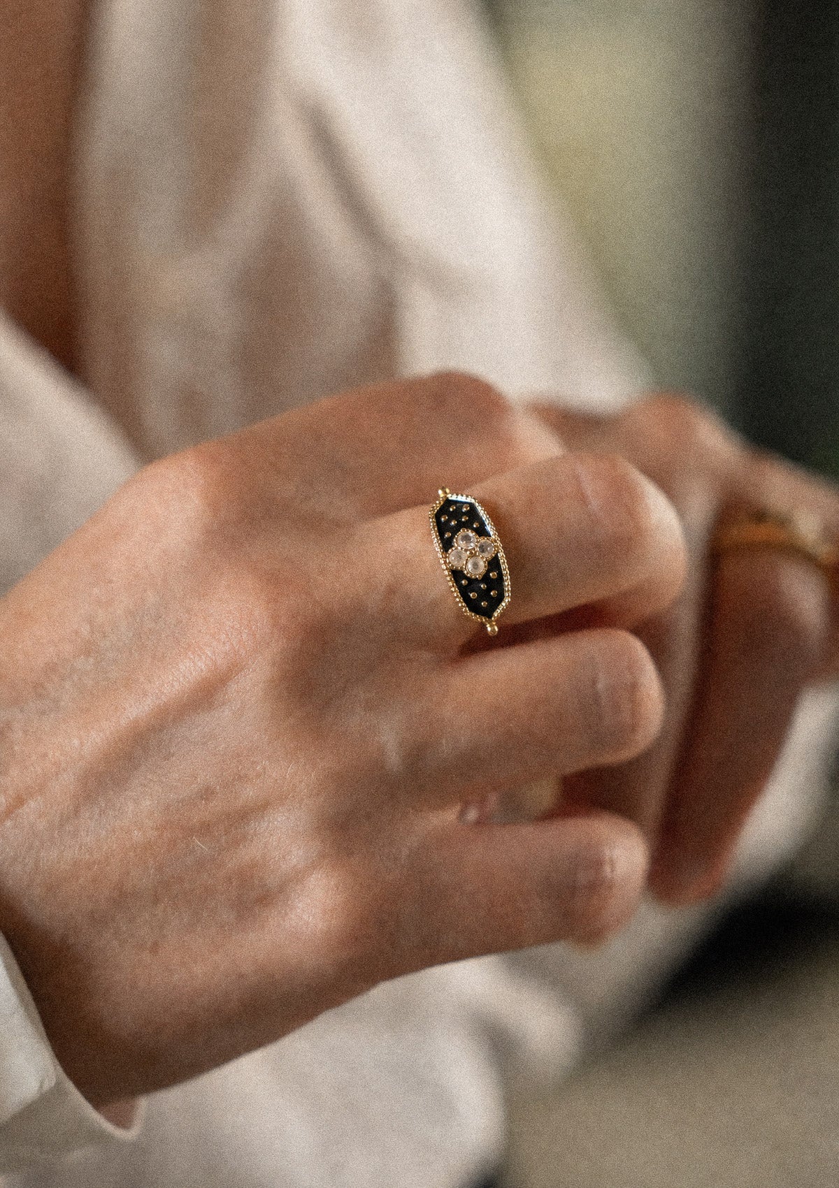 Bague plateau émail noir sertie quatre Pierres de Lune motif trèfle portée sur majeur main levée, pierre d'intuition et de féminité