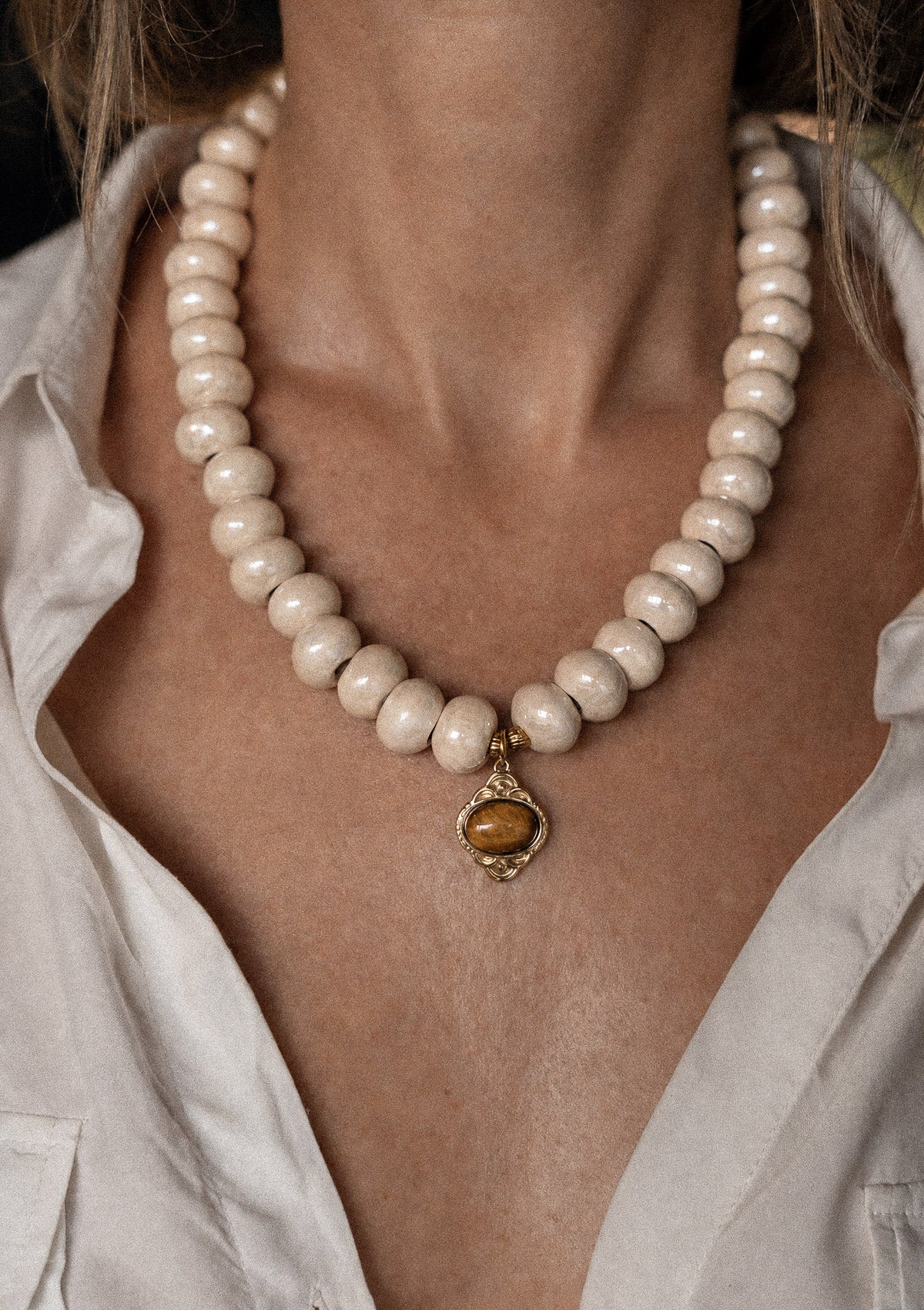 Collier ras-de-cou perles céramique émaillée et pendentif Œil de Tigre porté sur chemise blanche déboutonée, pierre de confiance