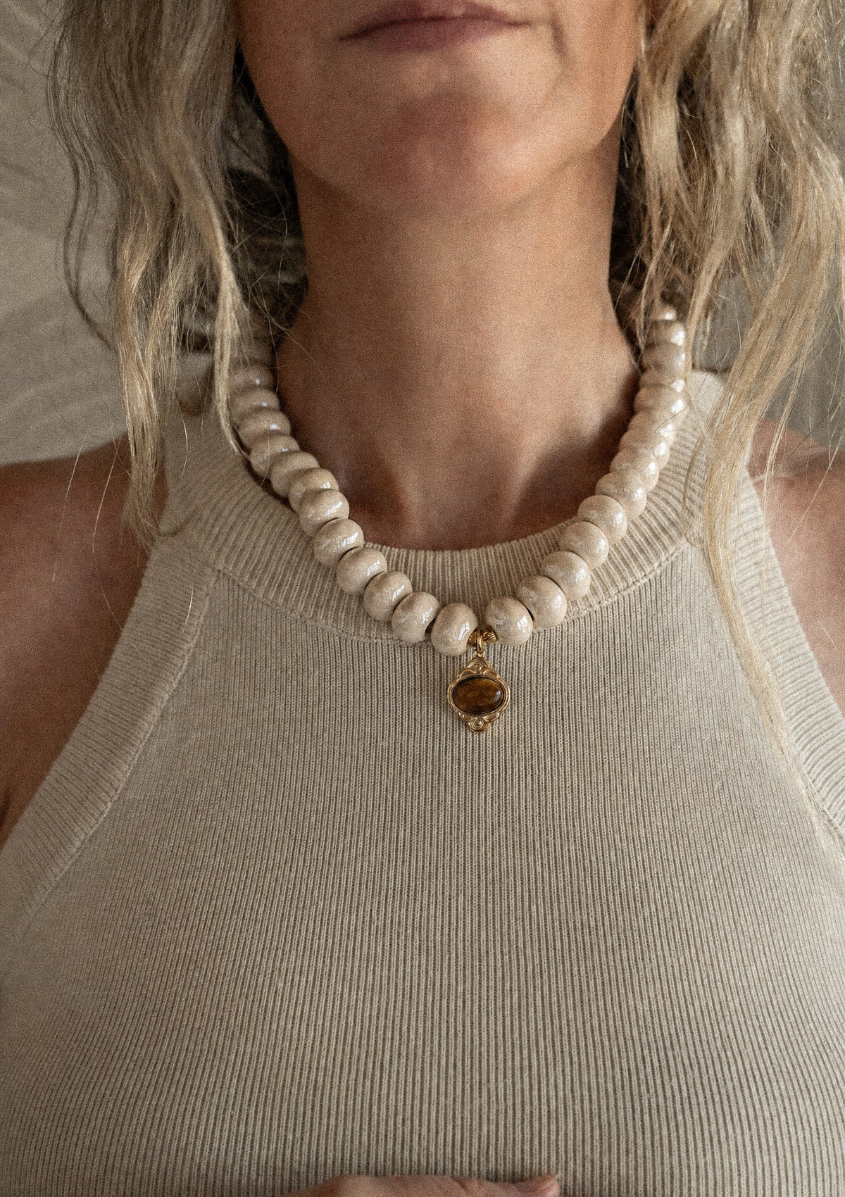 Collier perles rondes céramique crème et pendentif Œil de Tigre doré porté sur débardeur côtelé beige, assemblé en France