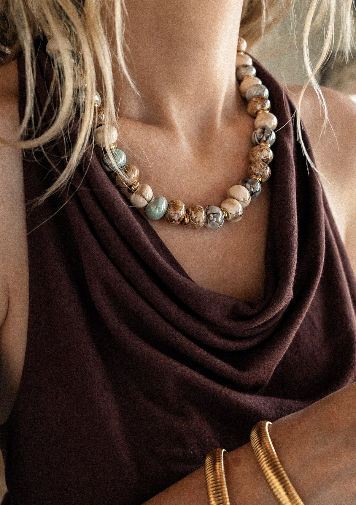 Collier ras-de-cou perles céramique émaillée porté sur top drapé velours marron chocolat, jonc doré au poignet, assemblé en France