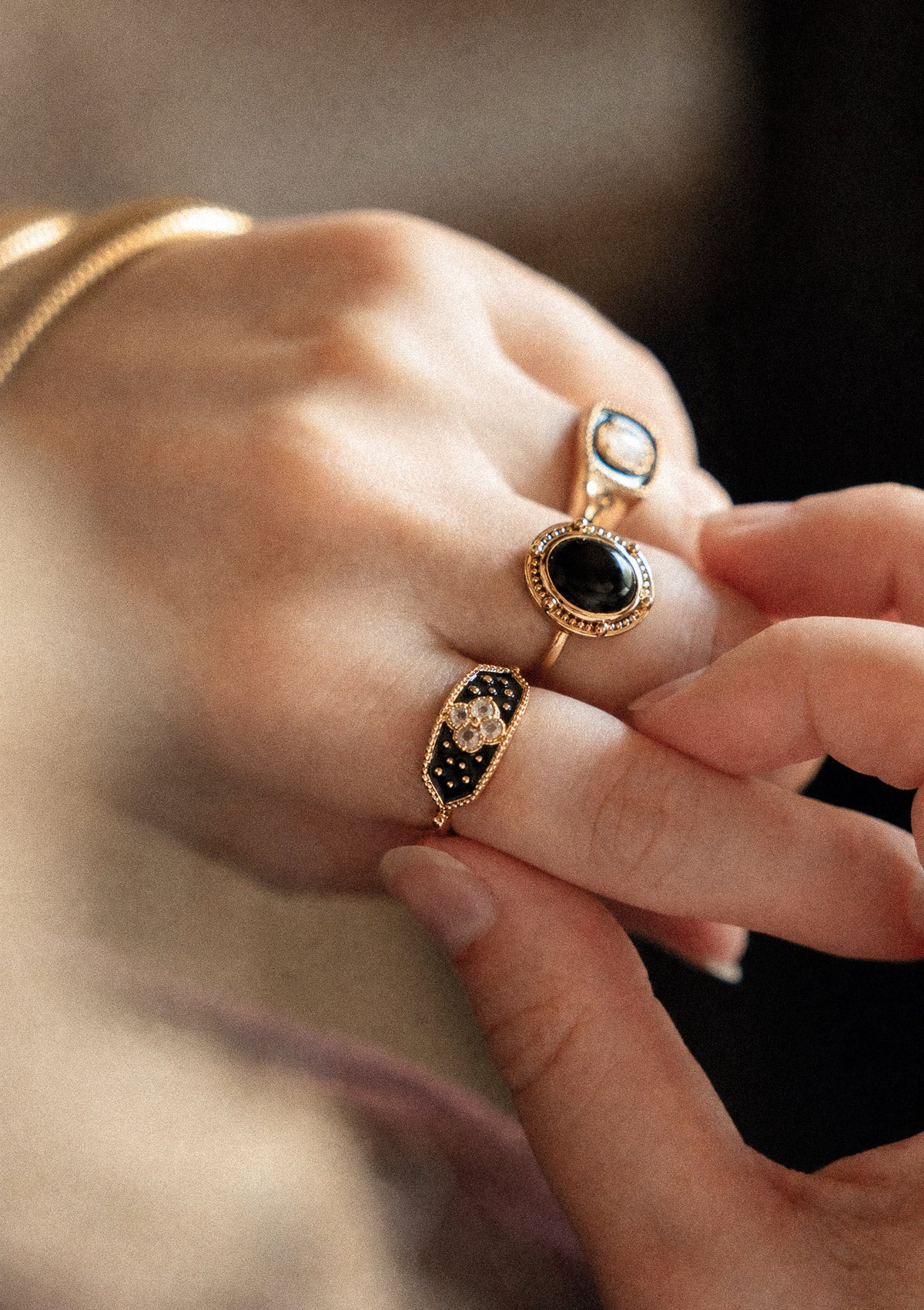 Deux bagues or recyclé 18 carats tenues main : bague ovale grande cabochon Onyx Noir contour perlé et plateau émail noir Pierres de Lune trèfle