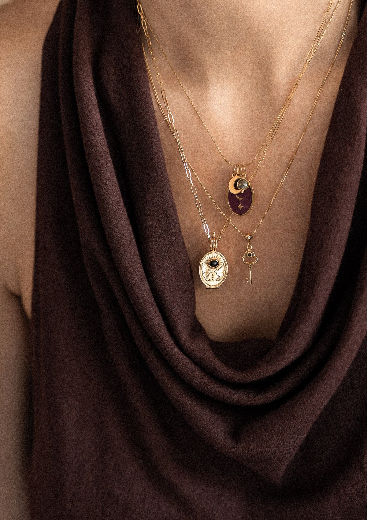 Trois colliers or recyclé 18 carats superposés sur drapé velours marron : paperclip Chemin se Révèle Onyx, chaîne fine Oracle Lunaire Pyrite émail bordeaux, mini clé Onyx
