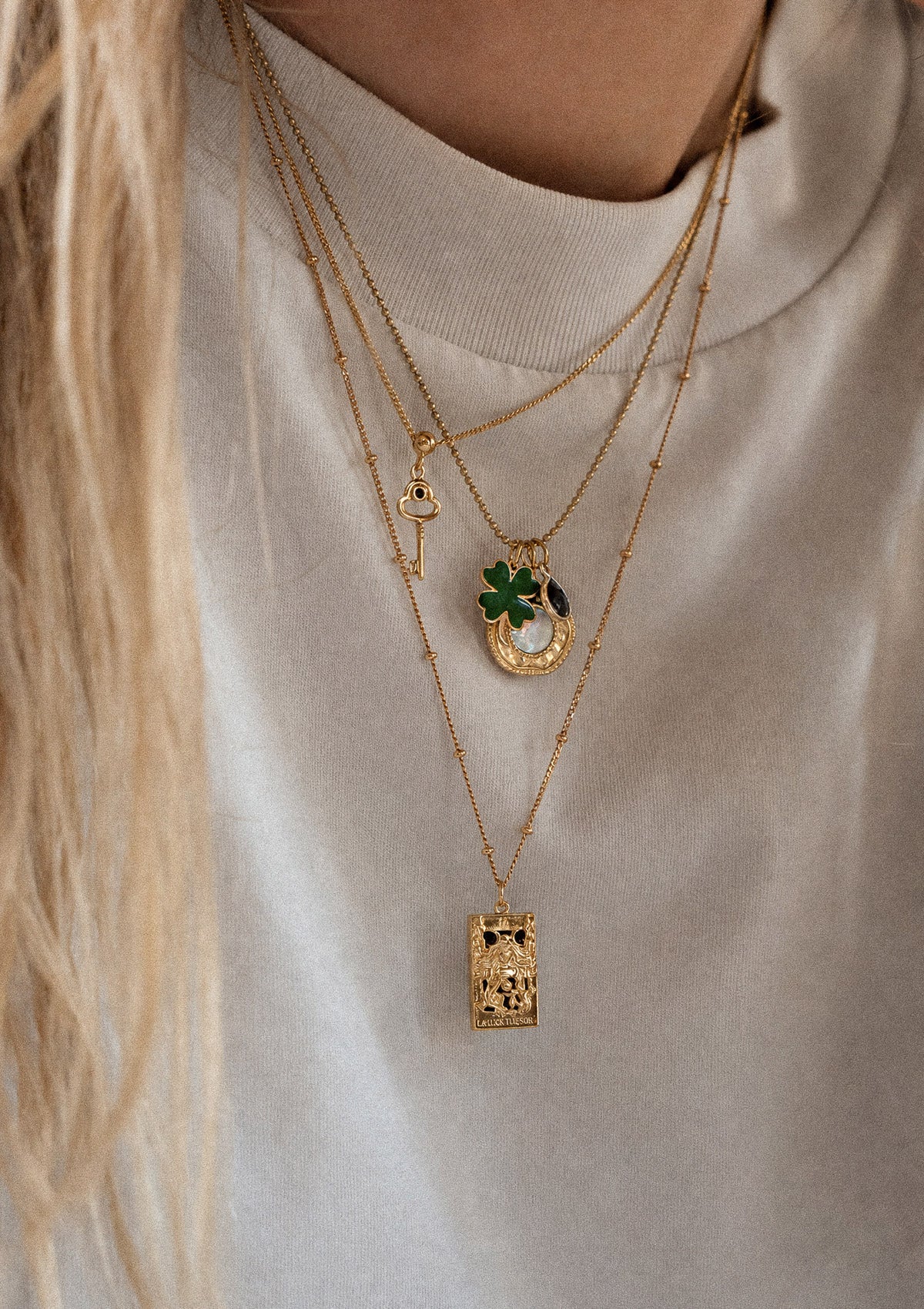 Accumulation trois colliers or recyclé 18 carats sur top beige tricoté : chaîne clé, charm Trèfle Nacre Onyx, pendentif tarot La Prêtresse