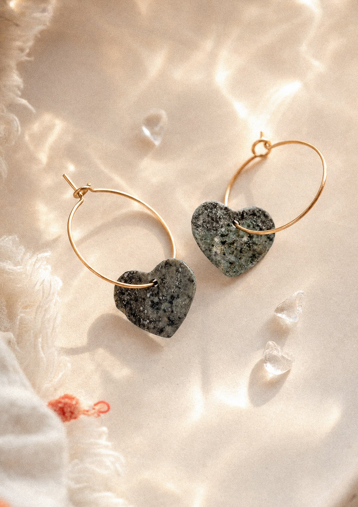 Créoles dorées à pendentif cœur en turquoise africaine verte mouchetée, pierre d'évolution et d'ouverture (chakra de la gorge) ; posées sur satin ivoire avec quartz brut – Namaka collection Solaire, assemblées en France