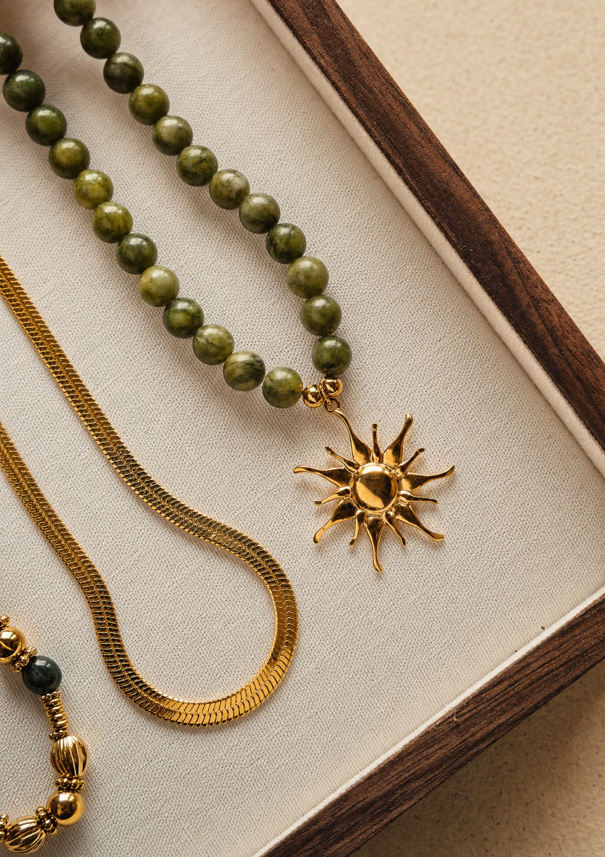 Collier Jade vert au pendentif soleil présenté avec un collier chaîne serpent Namaka, bijoux assemblés en France