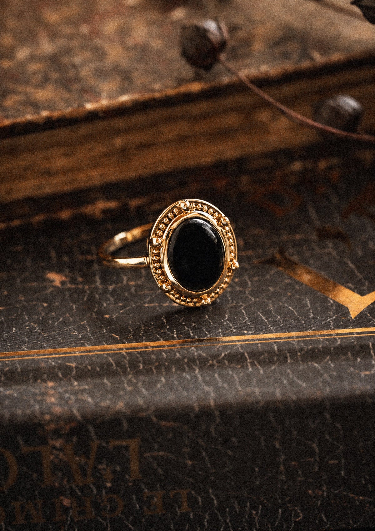 Bague or recyclé 18 carats sertie cabochon ovale Onyx Noir contour perlé sur livre relié cuir ancien, pierre de protection