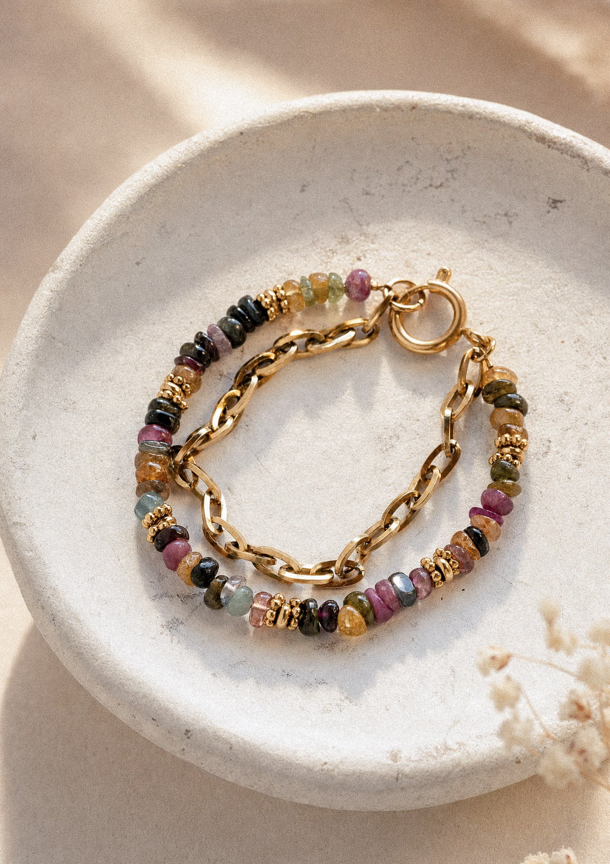 Bracelet Alliance Protectrice posé sur coupelle beige, double rang chaîne dorée et Tourmaline multicolore rose vert noir en accumulation – Namaka collection Solaire, assemblé en France