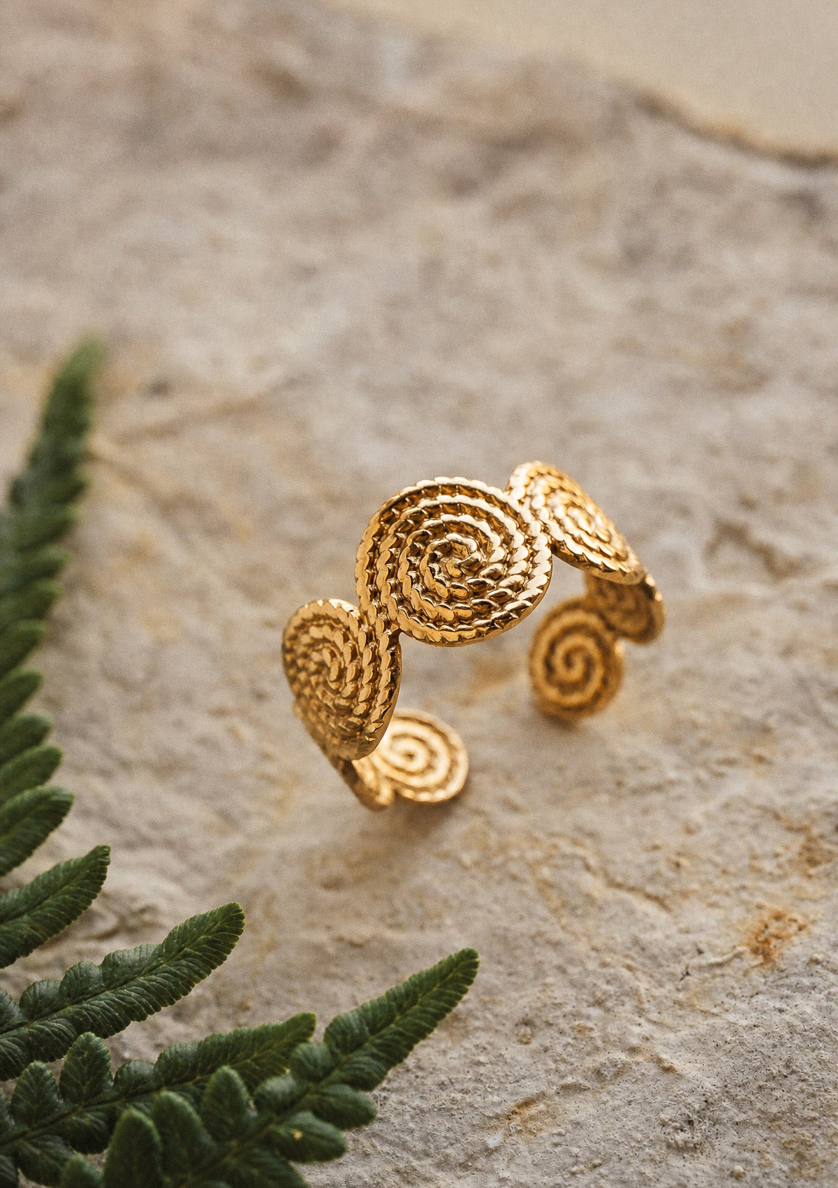Bague spirale dorée vue de profil sur fond minéral, anneau ajustable en acier inoxydable doré avec motifs en relief bohèmes signé Namaka