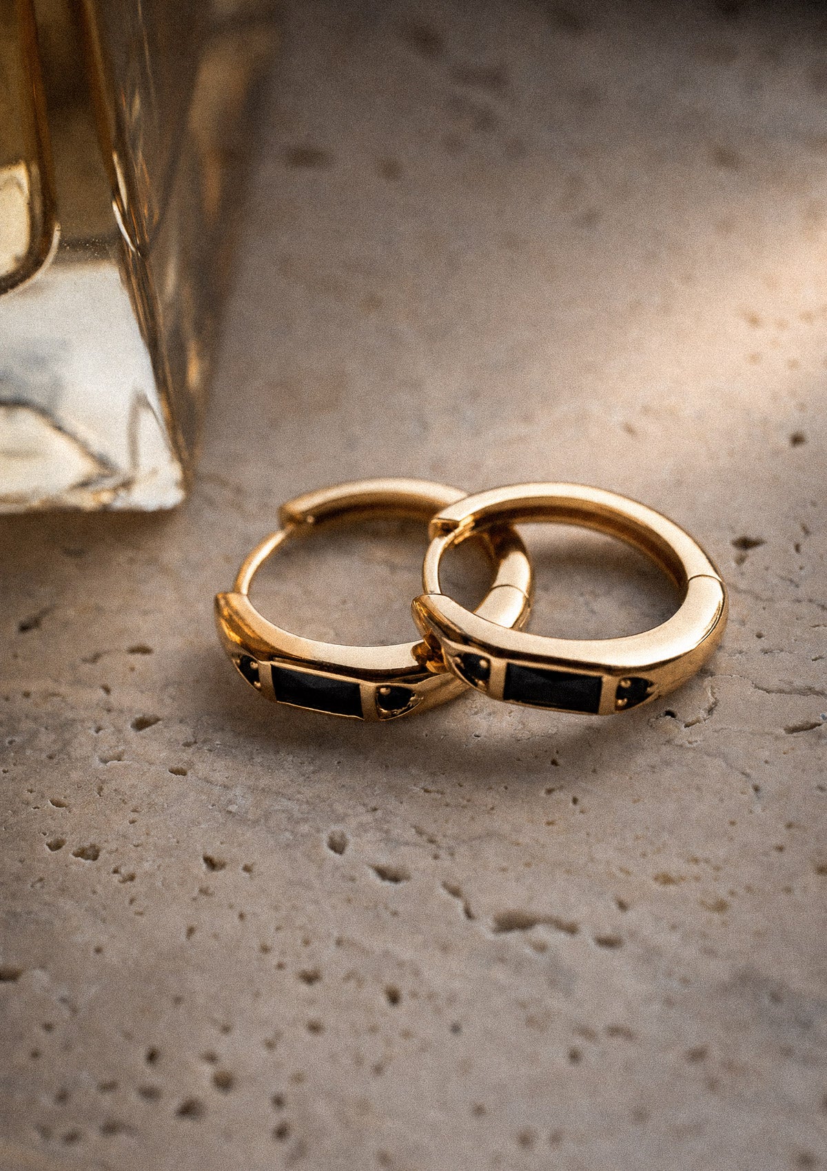 Deux créoles or 18 carats à barrette centrale Onyx Noir baguette et cabochons ronds, packshot sur pierre travertin