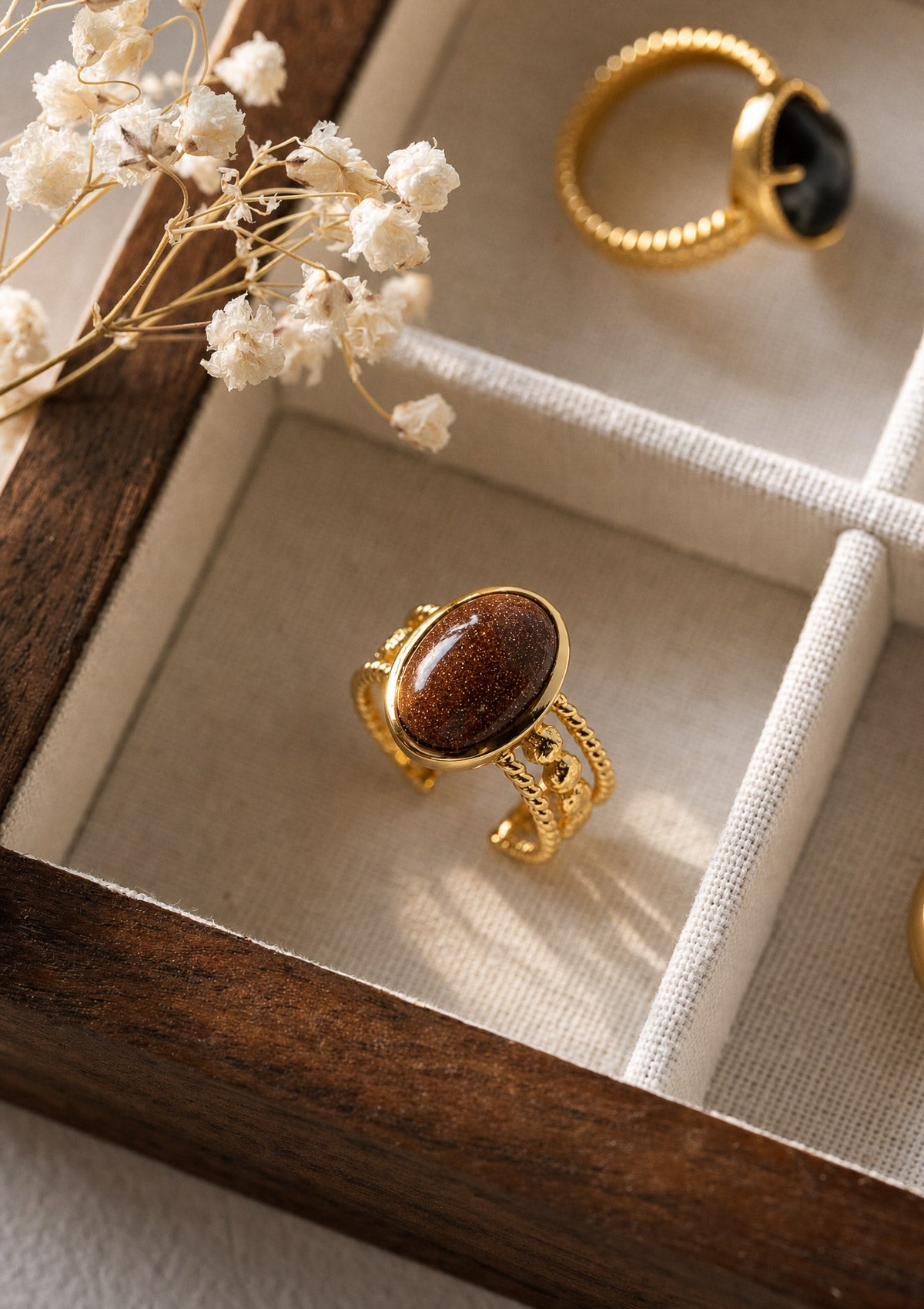 Bague Pierre de Sable présentée avec d'autres bagues Organica dans un écrin bois, anneau doré ajustable au cabochon scintillant Namaka