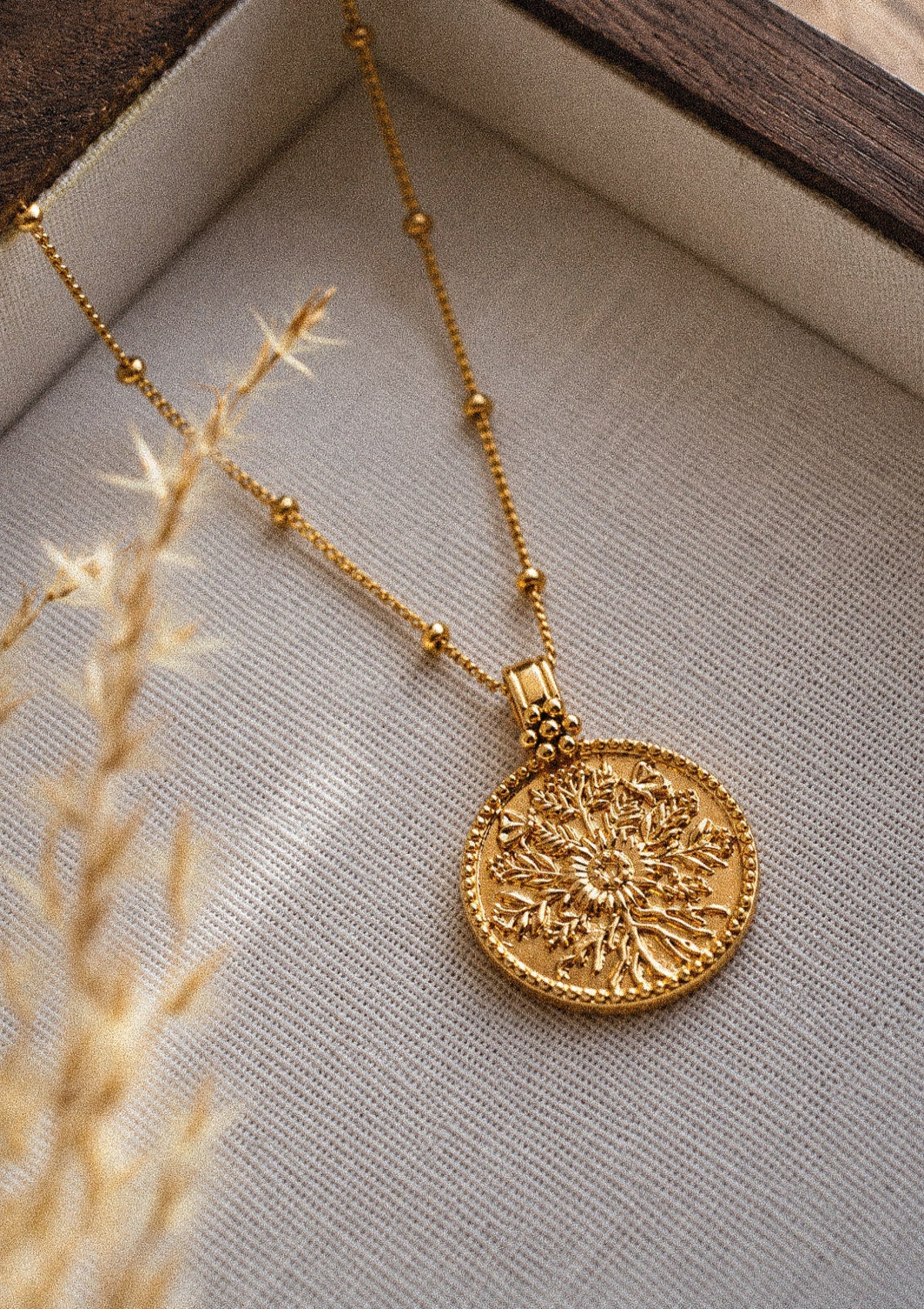 Médaillon doré sculpté en relief présenté avec mini créoles perlées dorées Namaka, inspiration bohème et symbolique