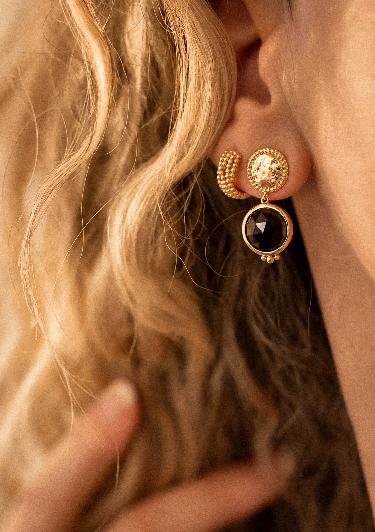 Détail des boucles d'oreilles Solaire Majestueuse portées à l'oreille, disque texturé doré et pendentif mobile en Quartz Fumé naturel Namaka
