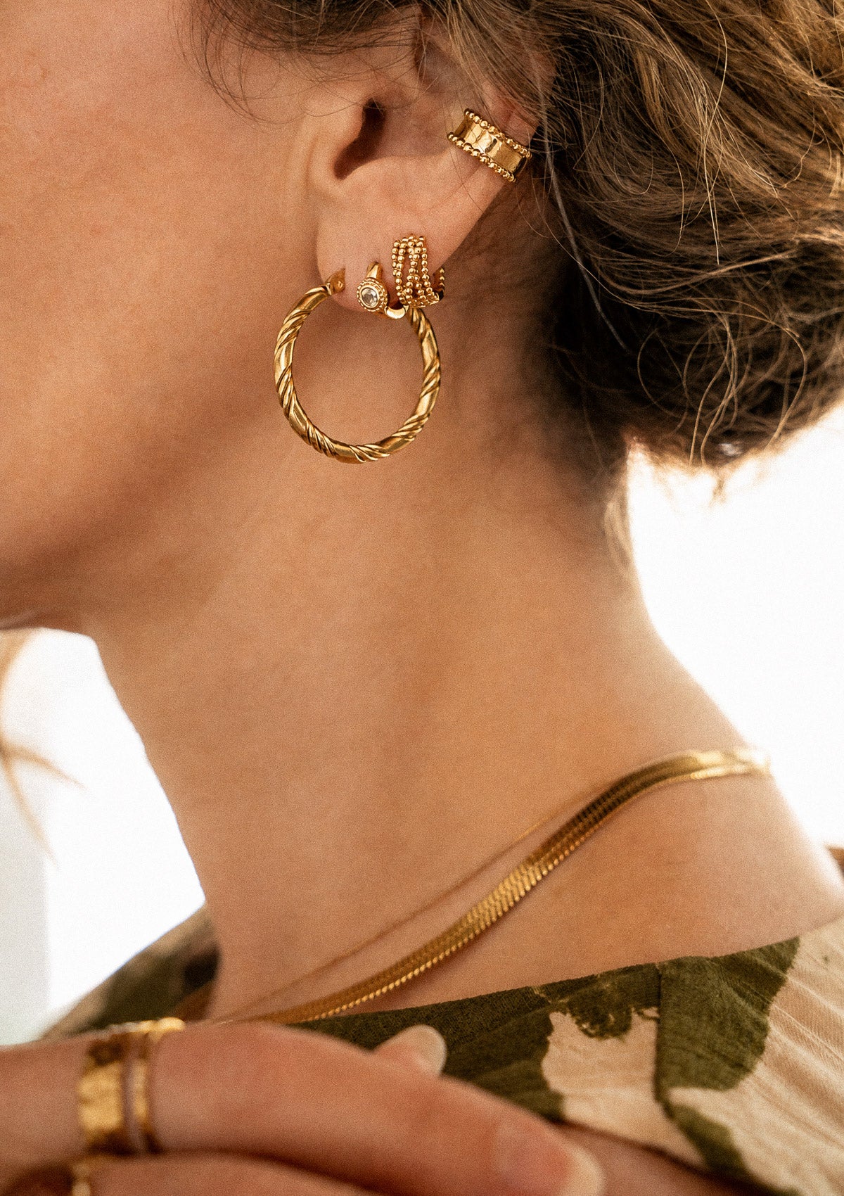 Grandes créoles torsadées Courant Libre portées à l'oreille en accumulation avec une mini créole Péridot et un ear cuff perlé Namaka