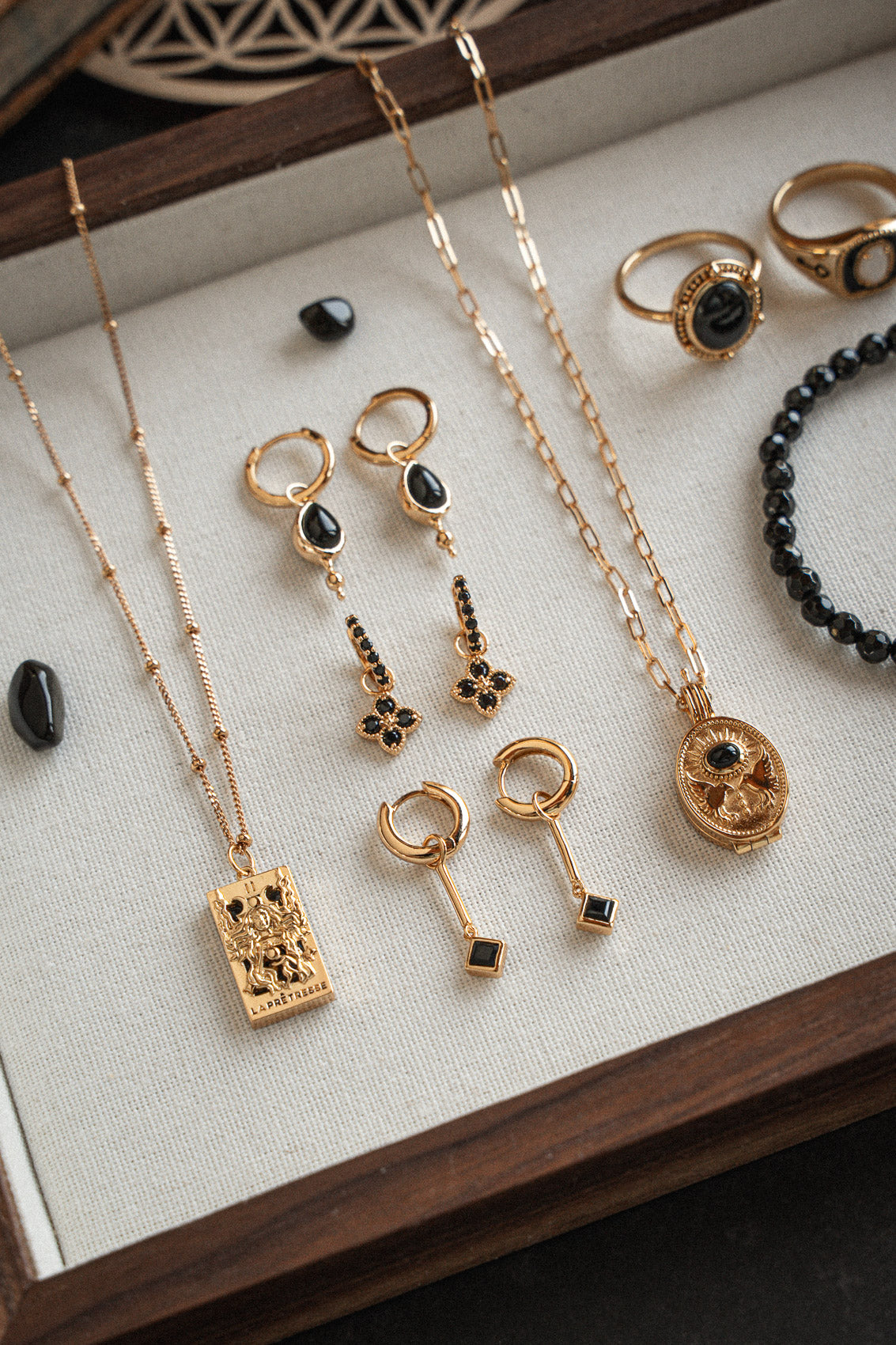 Bijoux or recyclé 18 carats et Onyx Noir sur plateau bois : collier tarot, créoles pampilles goutte, mini créoles fleur, chevalière, bracelet perles