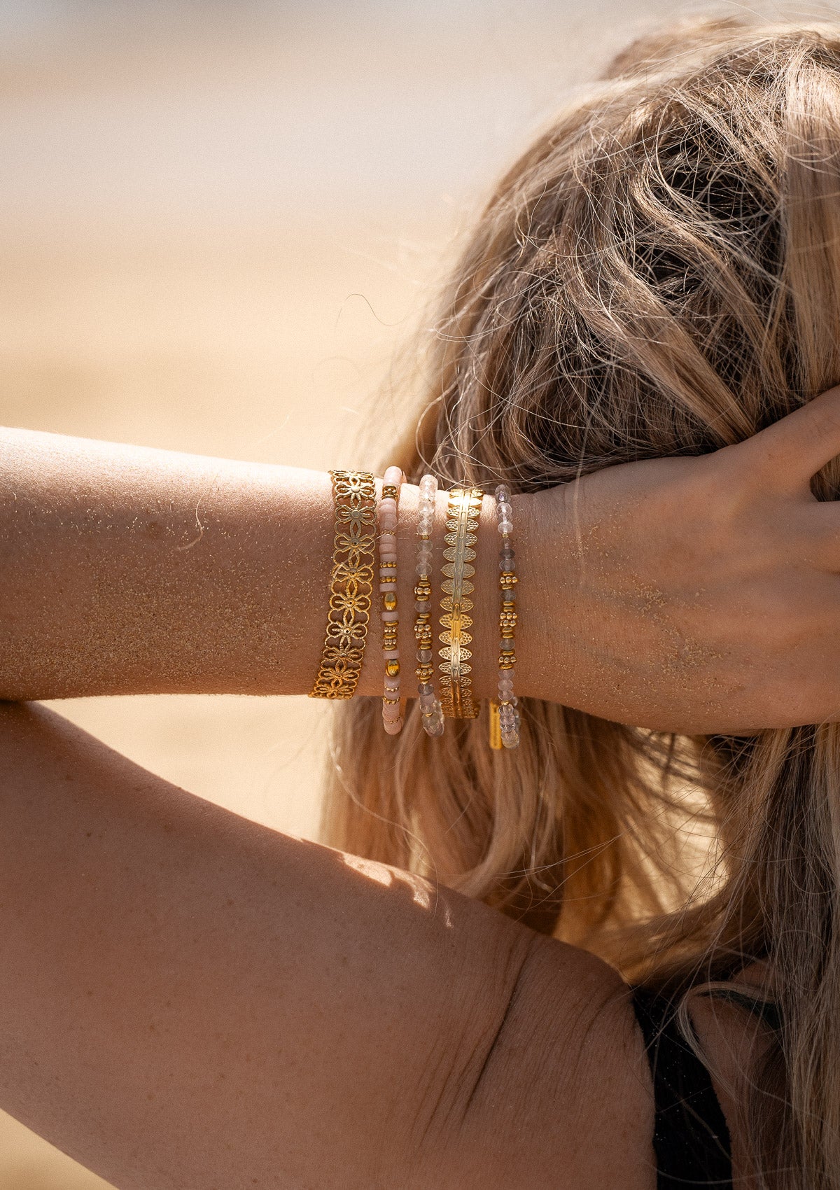 Accumulation de bracelets dorés et pierres naturelles sur peau sablée